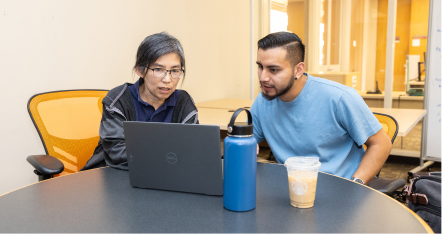 Research librarian providing instruction to a student with a laptop between then in the library consultation space